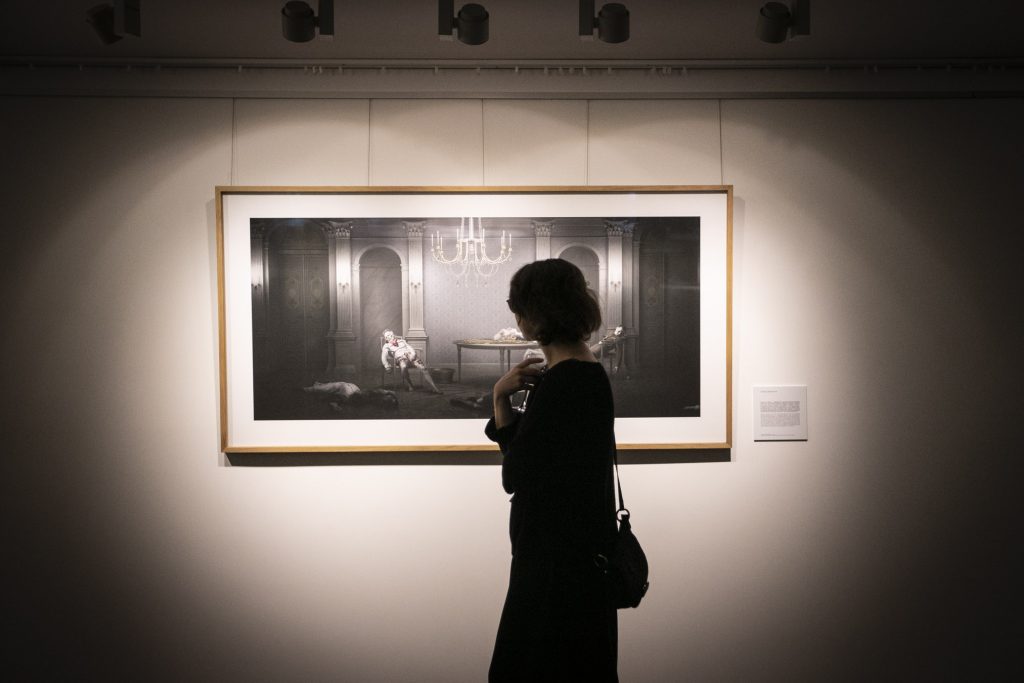 Kobieta ubrana na czarno stoi przed obrazem wiszącym na ścianie.