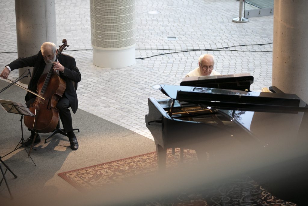 Koncert online. Na dolnym foyer siedzi dwóch mężczyzn. Jeden gra na fortepianie. Drugi z mężczyzn gra na kontrabasie.