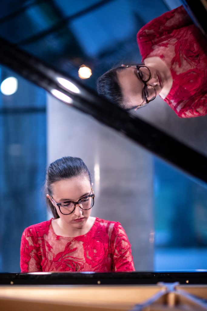 Koncert online transmitowany z dolnego foyer. Kobieta w czerwonej sukni gra na fortepianie.