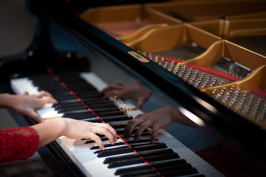 Zbliżenie na klawiaturę pianina na której gra kobieta w czerwonej sukni.