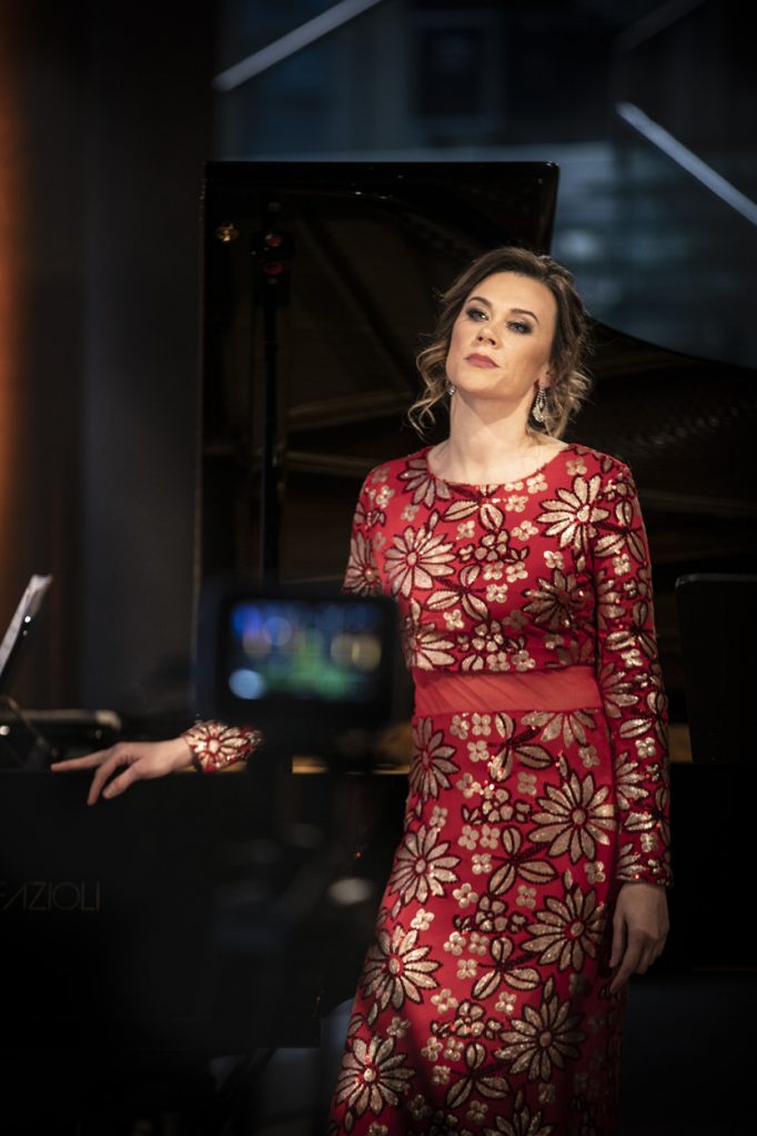 Koncert online z cyklu ''Jesień z Chopinem'' transmitowany z dolnego foyer. Przy fortepianie stoi kobieta w długiej, czerwonej sukni.