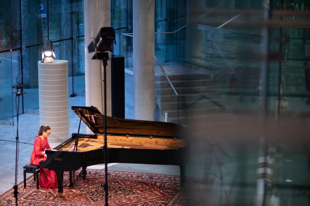 Zdjęcie zrobione z góry. Koncert ma dolnym foyer z cyklu ''Jesień z Chopinem''. Przy fortepianie siedzi kobieta w czerwonej sukni.