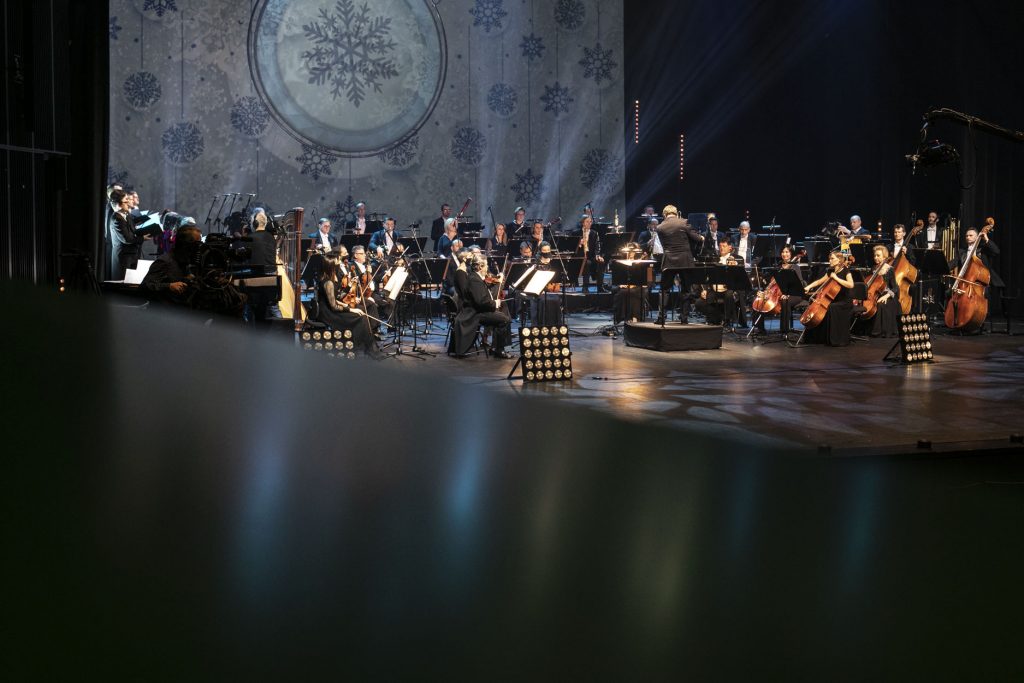 Duża Scena Opery i Filharmonii Podlaskiej na której nagrywany jest koncert ''Wielkie kolędowanie''. Na środku, na podeście stoi dyrygent. Dookoła siedzi Orkiestra Opery i Filharmonii Podlaskiej. Po prawej stronie, na wysięgniku kamera.