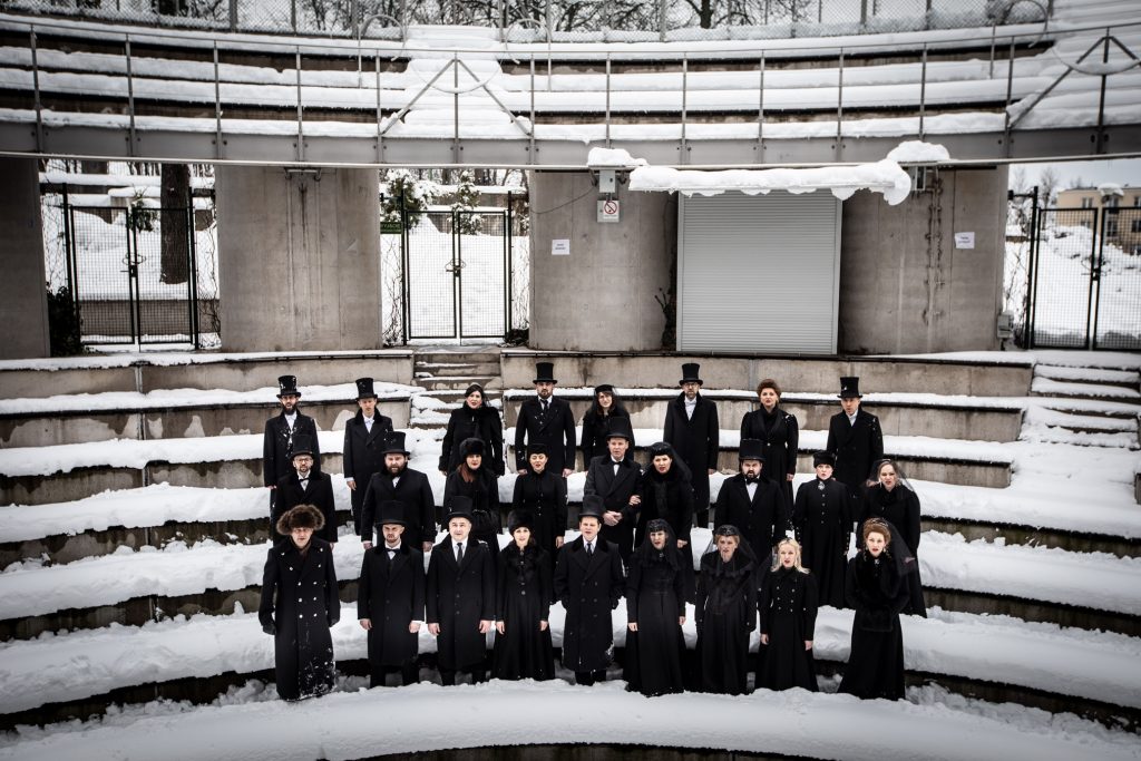 Widownia amfiteatru opery zimą .Kilkanaście osób ubranych na czarno stoi w śniegu pomiędzy rzędami.