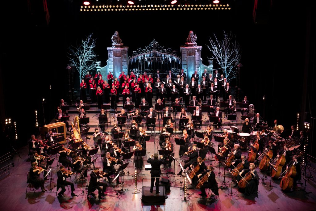 Koncert na Nowy Rok. Na scenie siedzi Orkiestra Opery i Filharmonii Podlaskiej. Za nimi, w dwóch rzędach stoi chór mieszany. Z przodu stoi dyrygent. Na końcu podświetlona, ozdobna brama. Po obydwu jej stronach drzewa bez liści podświetlone białym światłem.